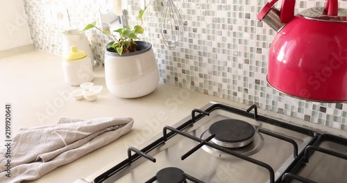 Lifting red kettle from gas stove. Modern domestic household kitchen appliances. Cozy morning routine beverage making.