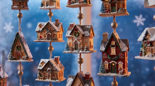 Miniature christmas village houses hanging on strings with snow and warm lights. Cozy holiday decoration on blue bokeh background.