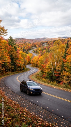 Black car driving on a winding road through autumn foliage  