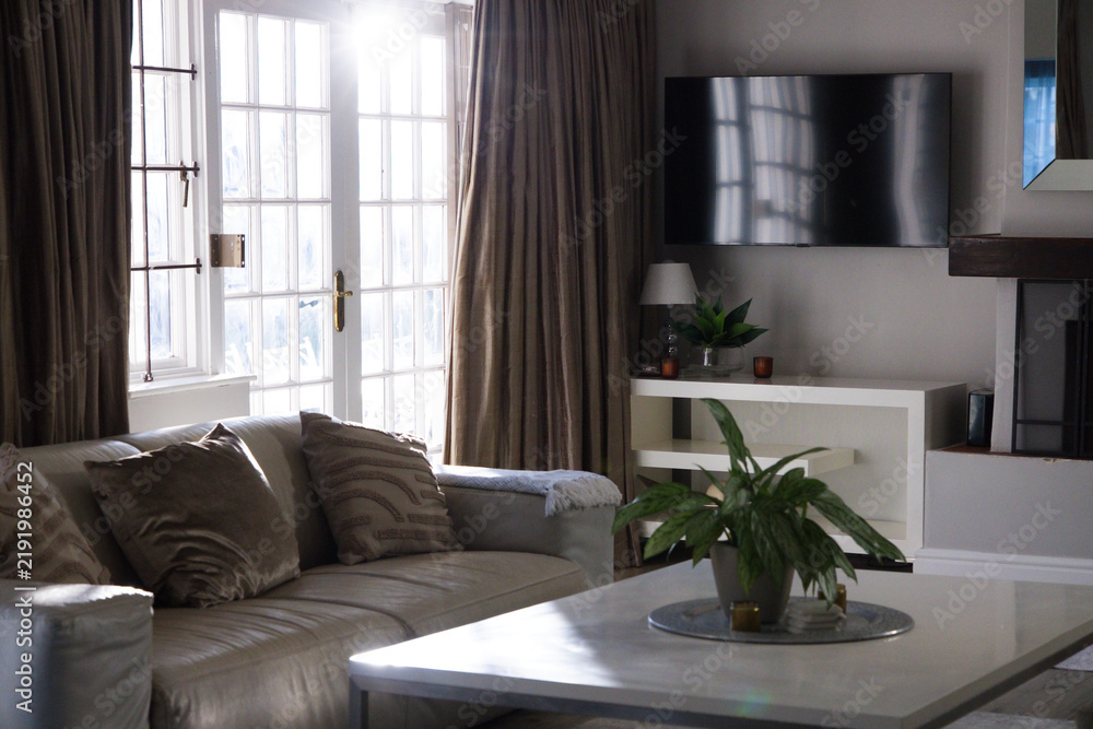Obraz premium Light-colored sofa is sitting left of center in living room near French doors with coffee table