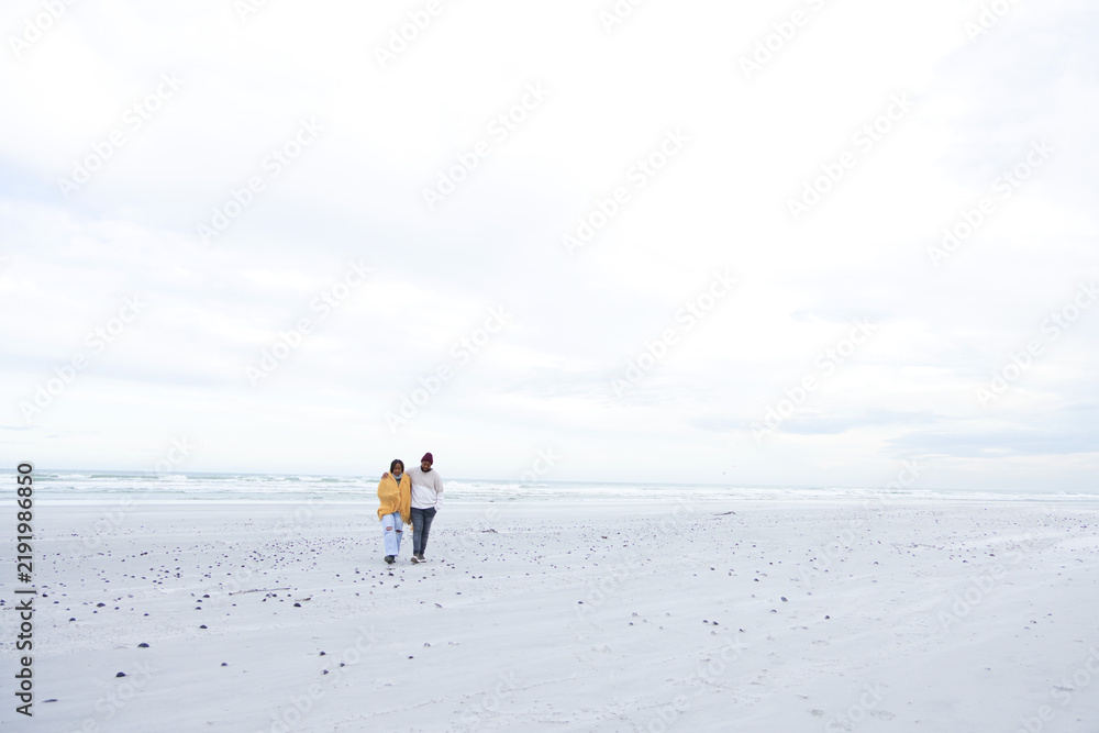 Obraz premium African American couple walking shore near ocean, stones prints, yellow jacket, burgundy beanie