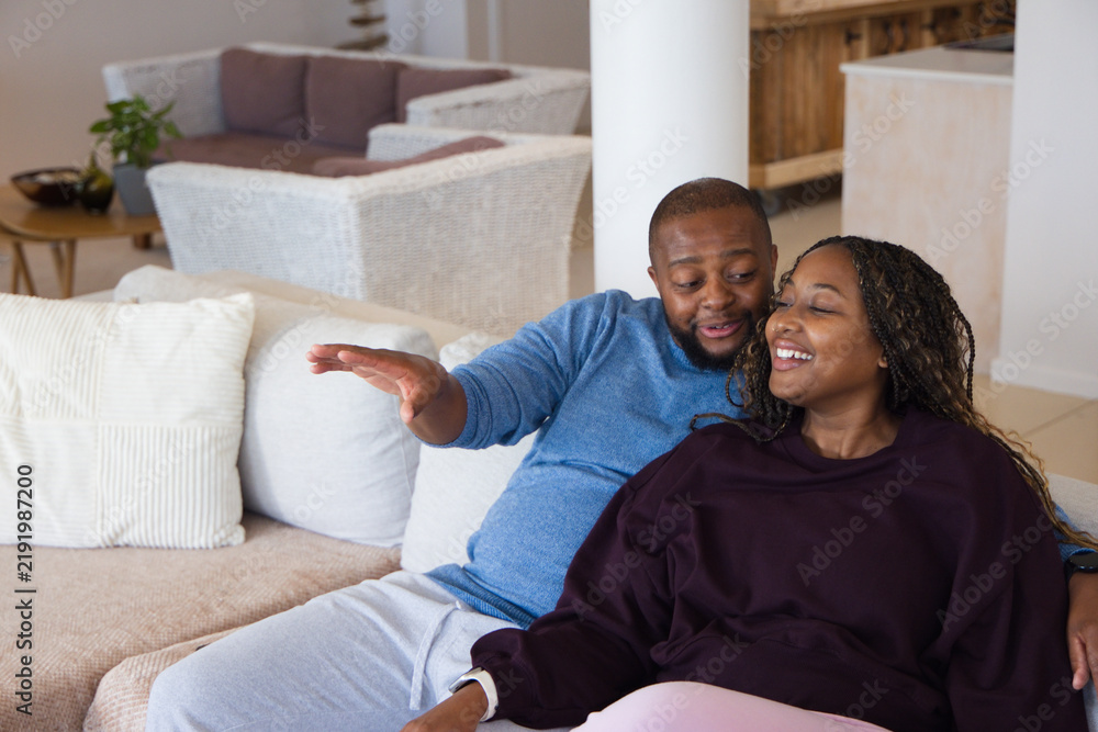 Obraz premium African couple sitting on sectional sofa at home, man gesturing, woman wearing watch, copy space