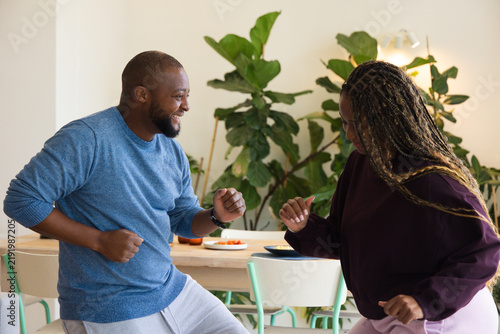 African American couple dancing in dining area by wooden table with sliced fruit and wristwatch