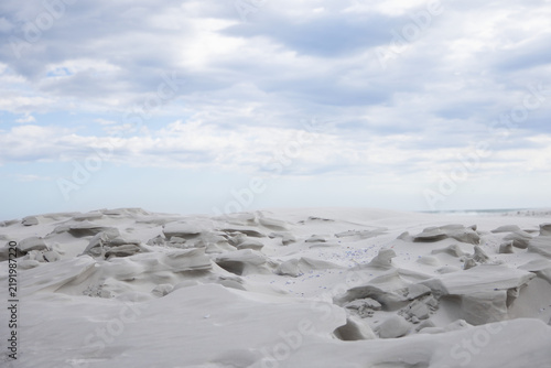 Wind-sculpted rocks are forming pebbled coastal sand flats with shallow hollows under cloudy sky
