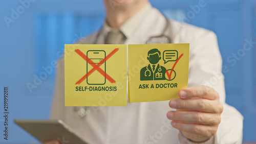 Doctor's hands holding yellow sticky notes showing a crossed out mobile phone for self diagnosis and an icon of a doctor for ask a doctor, emphasizing the importance of professional medical advice