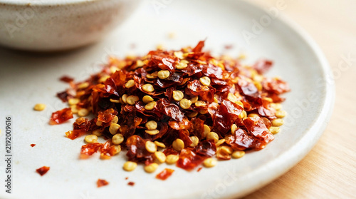 Vibrant crushed red pepper flakes with seeds piled on a minimalist ceramic plate, offering a spicy, aromatic culinary ingredient close-up.