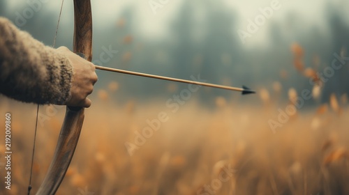 A young Caucasian adult male archer aims a wooden bow and arrow in a misty field
