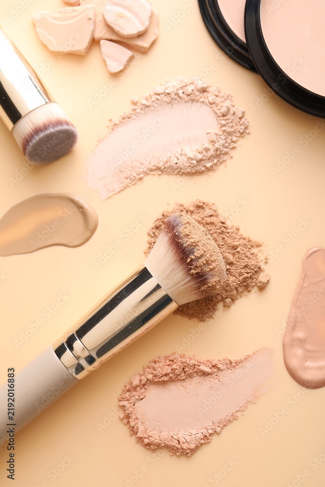 Obraz premium Swatches of different foundations, face powders and brushes on beige background, flat lay