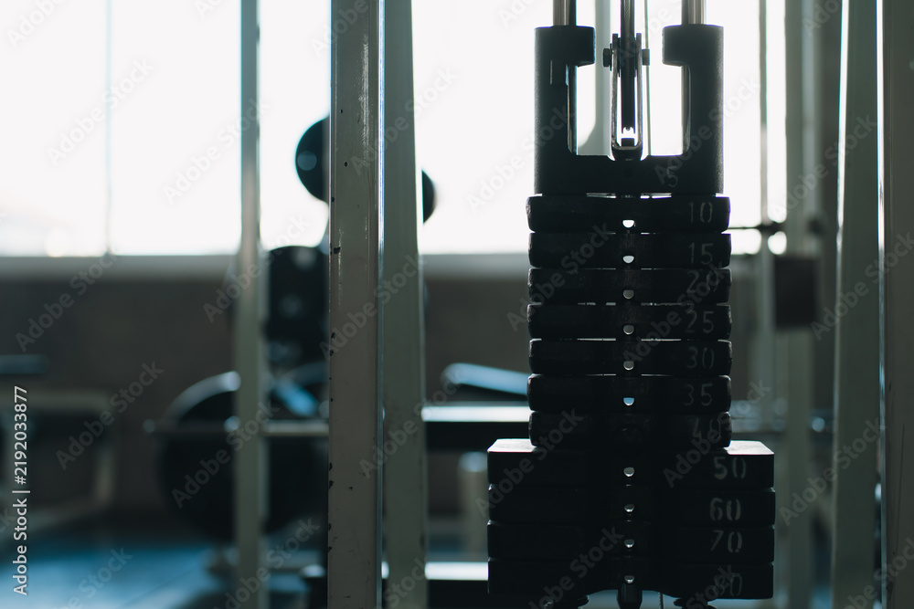 Obraz premium Weight plate cable machine gym equipment strength training setup with dark metal plates and blurred workout space, creating focused athletic atmosphere for fitness exercise