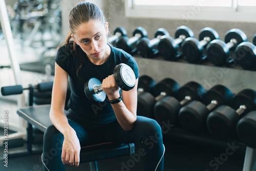 Fotografie Young woman exercising with dumbbell in gym, showing focused determination durin