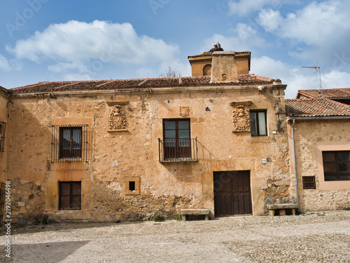 Historic Cobblestone Plaza in Spain - A view of an empty, traditional cobblestone plaza surrounded by ancient stone buildings with terracotta roofs and intricate architectural de