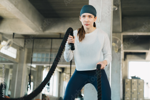 Obraz na plátně Athlete woman exercising with battle rope in modern gym for strength training an