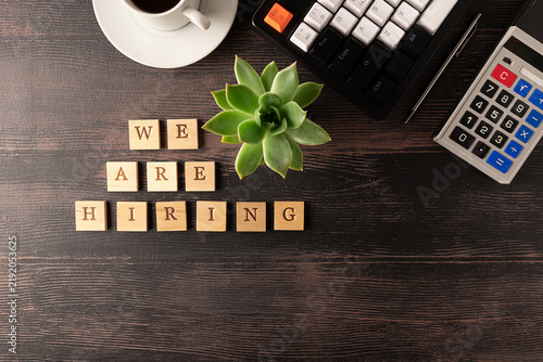 Office desktop with keyboard, succulent flowers, cup of coffee, vintage calculator and text We are hiring on the wooden cubes. Hiring and recruitment of staff concept. 