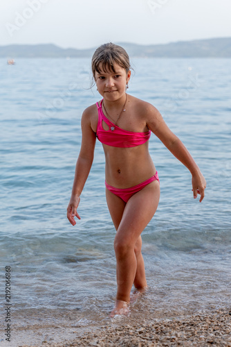 Young girl in pink bikini walking through shallow beach water