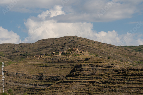 Картината върху платно Distant view of abandoned ghost village ruins on terraced mountain with wind tur