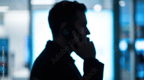 Blurred silhouette of a person speaking on a phone against a bright white and cool blue backlight, anonymous communication concept photography, strong dark profile, deliberate defocus, minimal