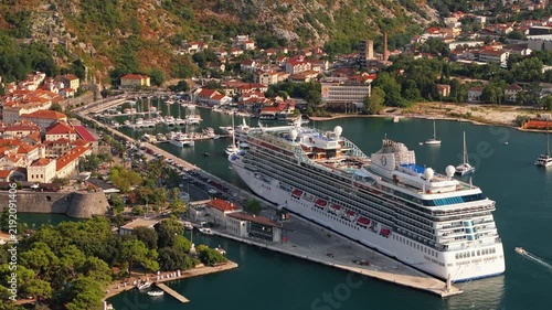 aerial tracking view of a large cruise ship berthed at the kotor cruise terminal beside the old town, marina and superyachts in warm late afternoon light, bay of kotor, montenegro