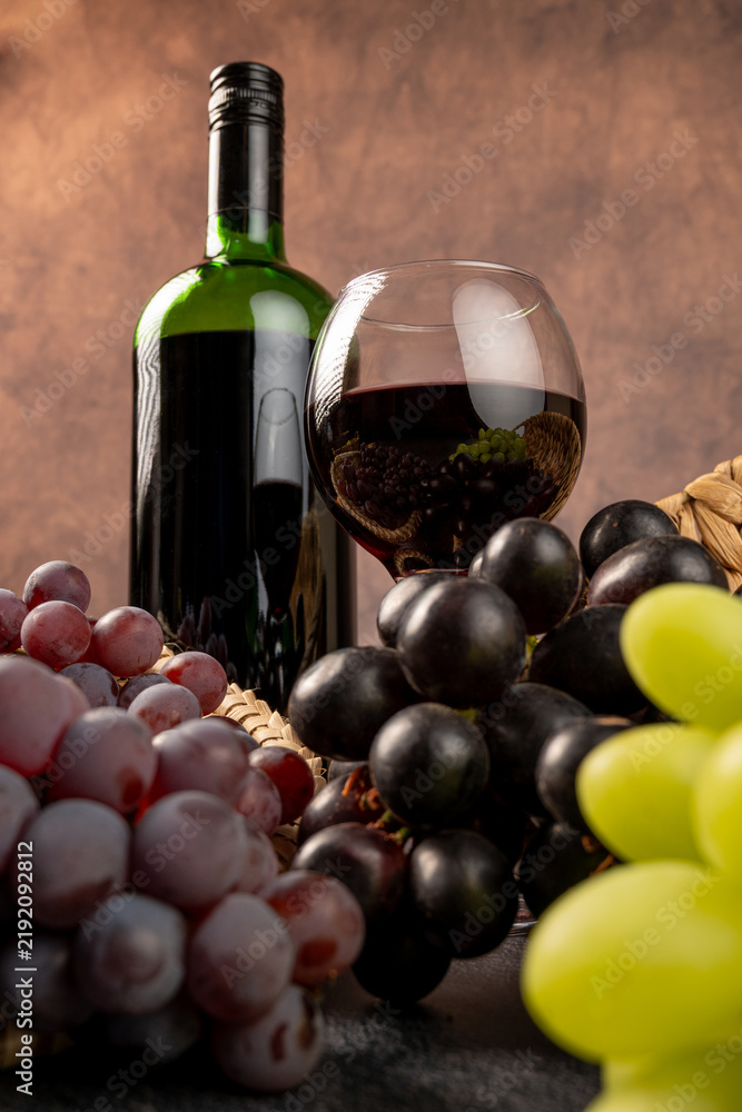 Fototapeta premium Arrangement of grapes and a bottle of red wine; beautiful grapes, a bottle of red wine, and accessories on a stone surface; abstract background, selective focus.