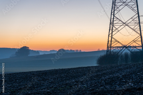 Electricity transmission tower over rural fields at dawn