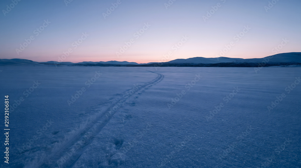 Fototapeta premium Snowy mountain landscape with ski tracks at sunset copy space