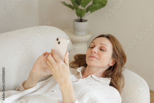 Woman Uses AI Voice Assistant on Smartphone While Relaxing at Home