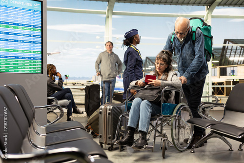 Konstfotografi Old man supports a woman in a wheelchair at the airport, embracing inclusion, accessibility and mobility support as the senior couple enjoys vacation travel and leisure despite limitations
