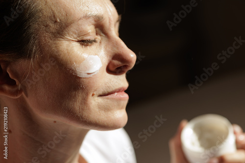 фотографія Mature Woman Applying Face Cream in Warm Morning Sunlight