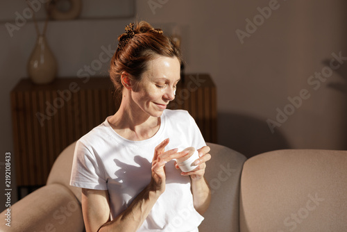 Принти на полотні Mature Woman Using Face Cream in Sunlit Morning Skincare Routine