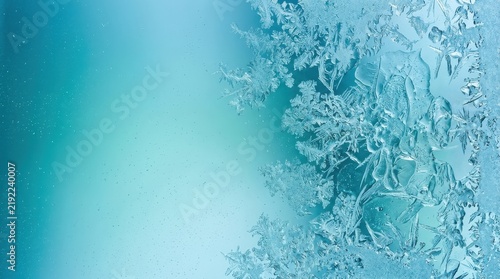 Intricate ice frost crystals forming beautiful patterns on glass window with soft blue gradient background for winter cold concept