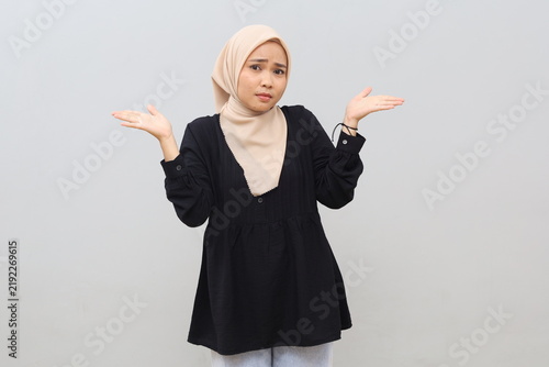 Cuadro en lienzo A confused Asian Muslim woman wearing a headscarf, unsure of what to do, shrugs her shoulders in hesitation—reflecting uncertainty—as she stands isolated against a white background