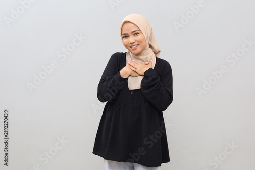 Obraz na plátně A young Asian Muslim woman wearing a headscarf appears touched and pleased as she receives a compliment; she has a cheerful, happy expression and is standing against a plain white background