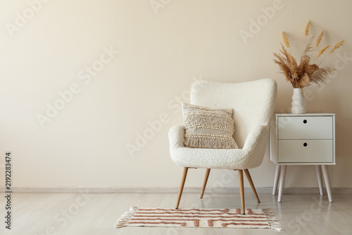 Comfortable armchair, chest of drawers and vase with pampas grass in living room