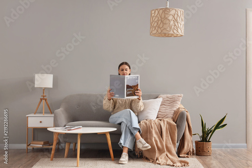 Young woman reading magazine on sofa with stylish lamps in living room