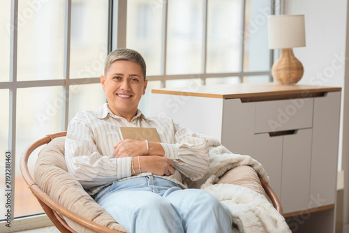 Young woman with short hair and book sitting in armchair at home