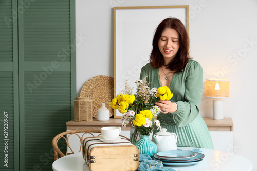 Young happy woman serving table with beautiful yellow flowers in dining room
