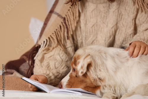 Owner with cute Australian Shepherd dog and book on bed in bedroom