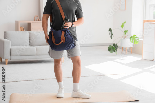 Man putting bottle of water into sports bag at home