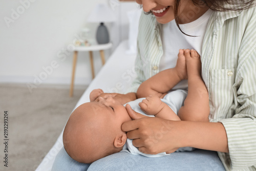 Beautiful young happy mother with her cute little baby sitting on bed at home...