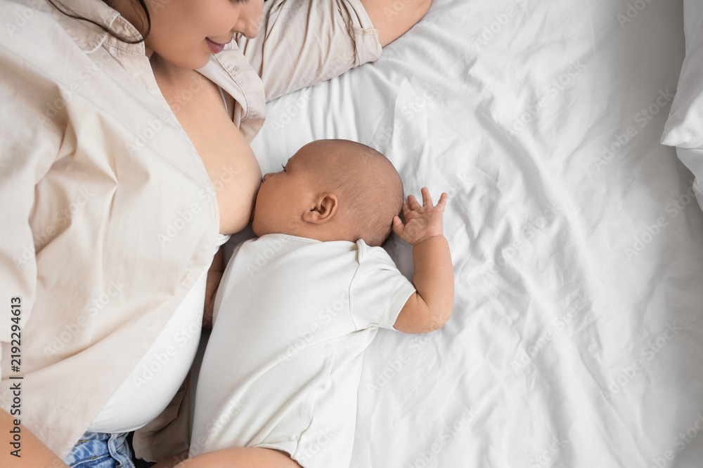 Obraz premium Young mother breastfeeding her baby on bed, top view