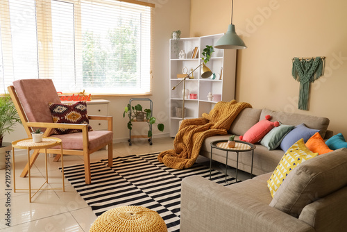 Comfortable sofas, armchair and tables near window in interior of living room