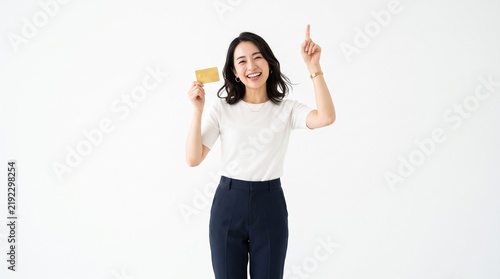 Happy young Asian woman smiling and pointing upwards while holding a gold credit card against a clean white studio background