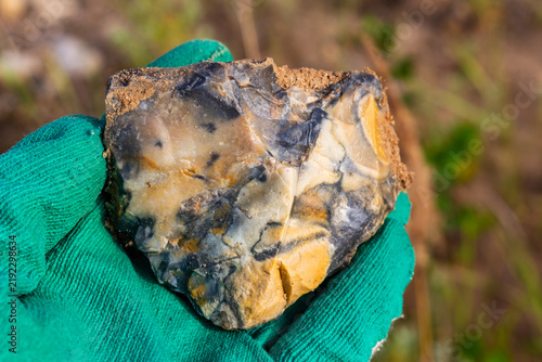 Картината върху платно Hand holding a rough, multi-colored flint stone fragment extracted from a quarry