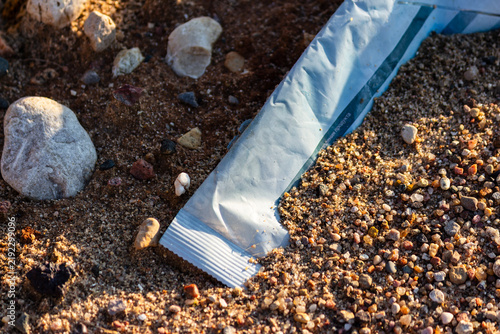Fotografie Discarded wet wipe packet lying among pebbles and sand, closeup of environmental