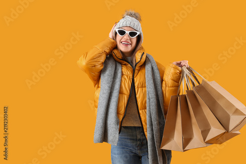 Pretty young woman with shopping bags on yellow background