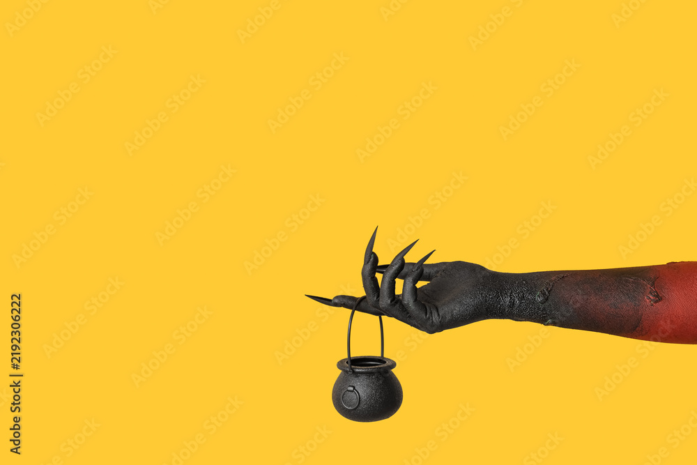 Obraz premium Black hand of witch with cauldron on yellow background. Halloween celebration