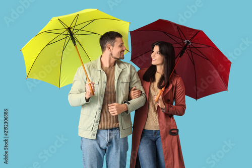 Young couple in autumn clothes with umbrellas on blue background