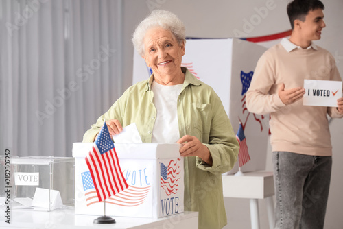 Fotografie Voting senior woman near ballot box with USA flag at polling station