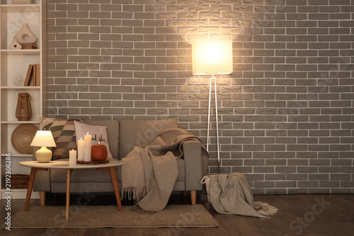 Cozy sofa, coffee table, shelving unit and glowing lamps in interior of livin...