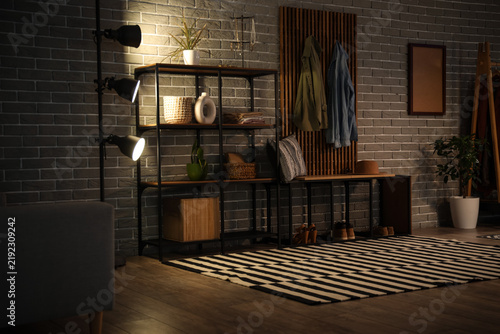 Interior of hall with glowing lamp, coat rack and shelves in evening