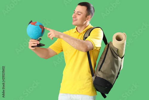 Male tourist with globe and bag on green background